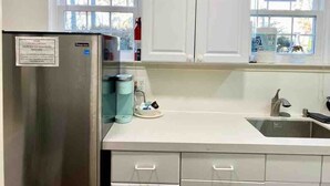 A kitchen with white cabinets, a stainless steel refrigerator, a sink, and a window with a view of the neighborhood. - Efficiency Bright BSMNT APT- DC 20m IAD-10m Metro (Reston)
