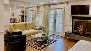 A living room with a sofa, a glass coffee table, a fireplace, and a television. - Efficiency Bright BSMNT APT- DC 20m IAD-10m Metro (Reston)
