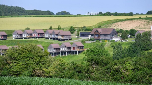 A row of wooden cabins with a grassy field and trees in the background.