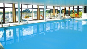 Una piscina interior con paredes de vidrio transparente, tumbonas y vistas del paisaje circundante.
