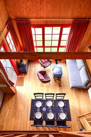 A wooden cabin interior with a dining table set for four, a sofa, and a small table with a chair.