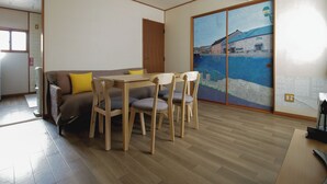 Ein Zimmer mit Holzboden, einer Couch mit Kissen, einem Esstisch mit Stühlen und einem großen Gemälde an der Wand.