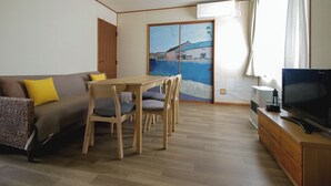 Ein Wohnzimmer mit einer Couch, einem Holzesstisch, Stühlen, einem Fernseher und einer Glastür mit Blick auf die Stadt.
