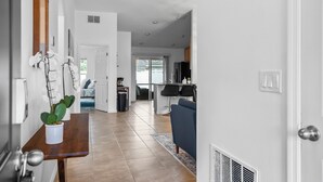 Et moderne køkken med et sort køleskab, et spiseområde med en blå sofa, og en gang med et træbord og potteplanter.