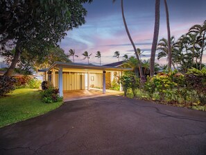 Une maison dotée d’un porche abrité, entourée d’une végétation tropicale et de palmiers.