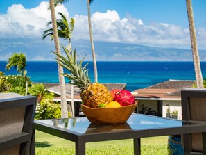 Une table avec un panier de fruits et une vue sur l’océan et les palmiers.
