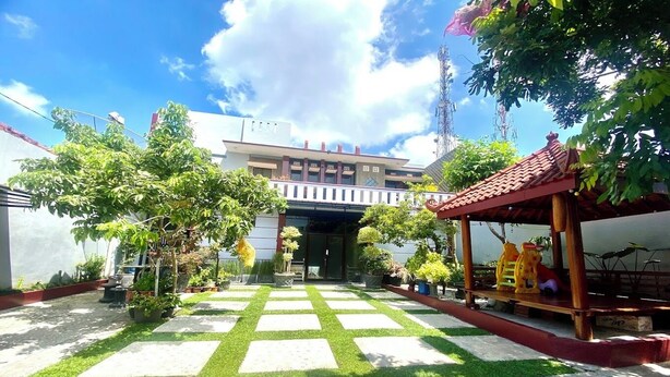 A courtyard with a checkered pattern of grass and stone, surrounded by potted plants and a wooden pavilion. - Berkah Syariah (Kutoarjo)