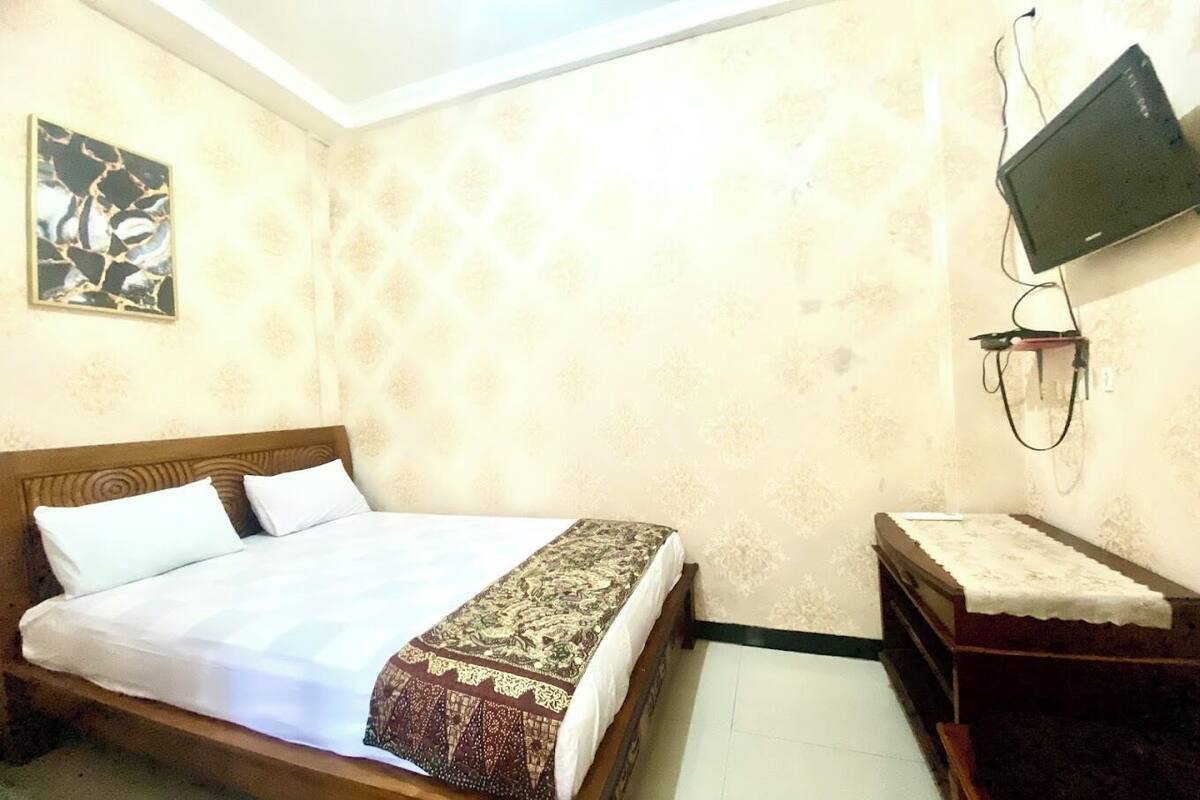 A bedroom with a bed, a TV mounted on the wall, and a small wooden dresser.