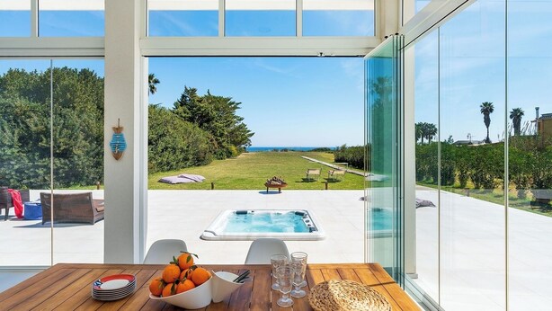 Ein modernes Zimmer mit einer großen Glasdoor, die auf eine Terrasse mit Whirlpool und Gartenmöbeln führt.
