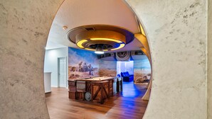 A pool table in a room with a desert mural, a door, and blue chairs.
