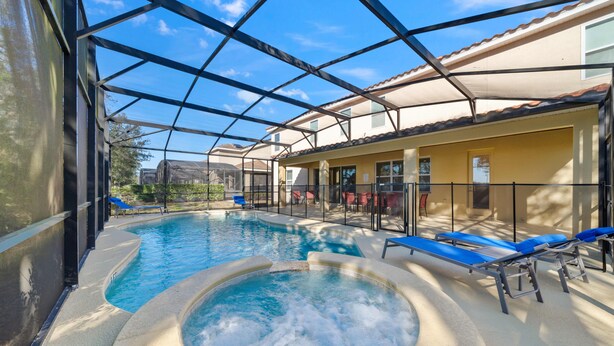 A swimming pool with a hot tub, sun loungers, and a covered patio area.