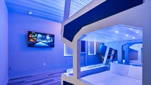 A modern hotel room with a bunk bed, a flat-screen TV mounted on the wall, and a wooden floor.