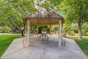 A gazebo with a metal roof and wooden beams, surrounded by a concrete base and metal railing.