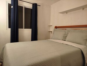 Ein Hotelzimmer mit Bett, einem Vorhangfenster, einem Holz-Kopfteil und einem Regal über dem Bett.