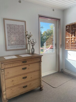 A wooden dresser with drawers, a framed artwork titled 'LEAVES & FLOWERS', and a window with a view of greenery.