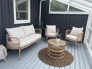 A covered outdoor seating area with a sofa, two chairs, a round table, and a potted plant.