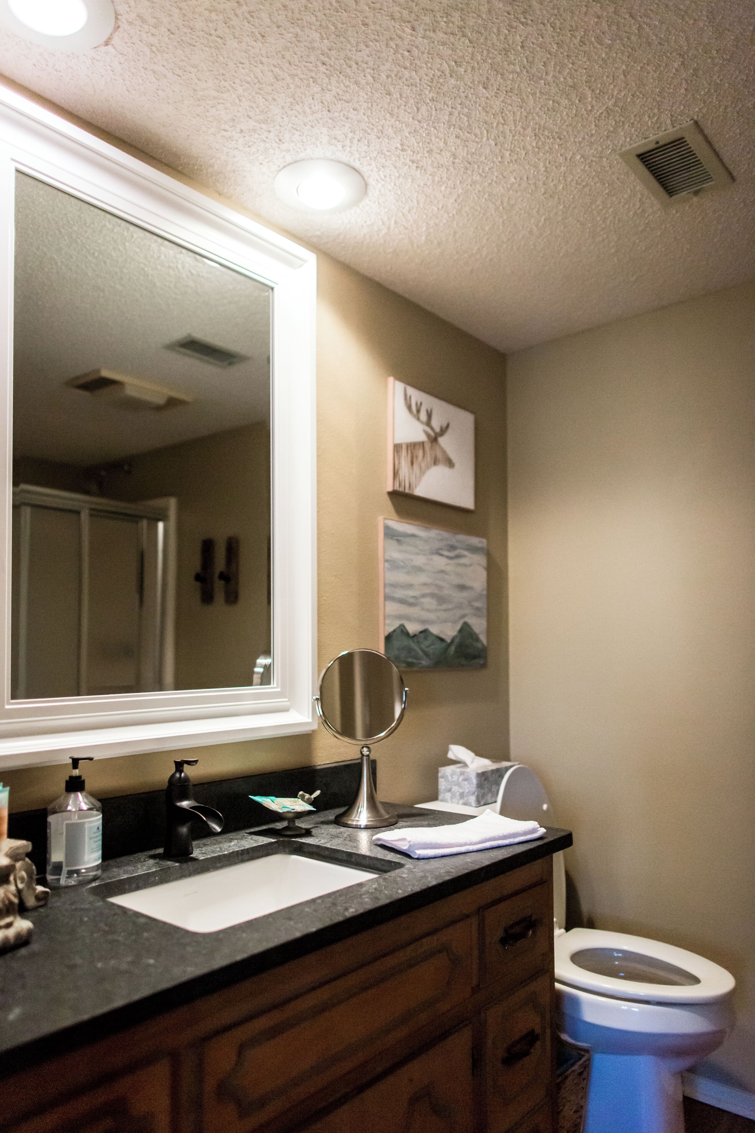 A bathroom with a large mirror, a sink, a toilet, and a cabinet.