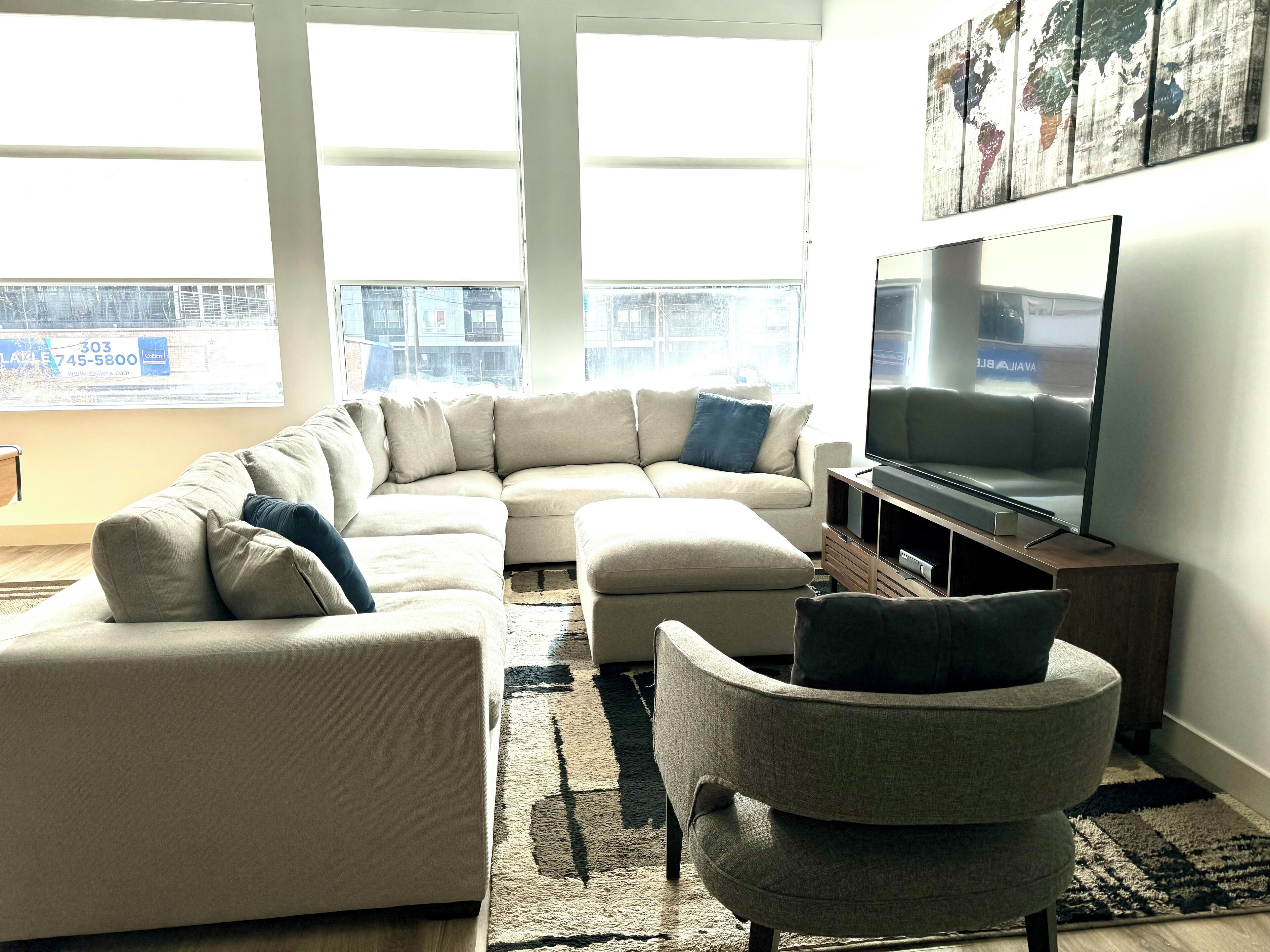 A modern living room with a large L-shaped sectional sofa, a grey armchair, and a flat-screen TV on a wooden stand.