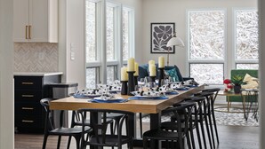Un coin repas avec une table en bois dressée pour six personnes, des chaises noires et une vue sur l’extérieur grâce à de grandes fenêtres.