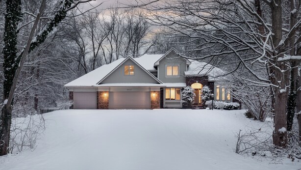 Une maison à deux étages avec un garage, entourée d’arbres couverts de neige et d’une pelouse bien entretenue.