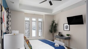 Une chambre moderne avec un lit, un bureau, une télévision et une fenêtre équipée de stores.