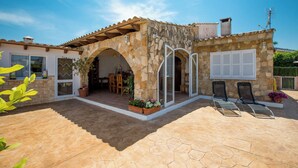 Un bâtiment en pierre doté d’un patio carrelé, d’un espace extérieur aménagé pour s’asseoir et d’une entrée couverte.