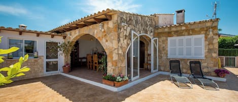 Un edificio de piedra con patio de baldosas, asientos exteriores y entrada cubierta.