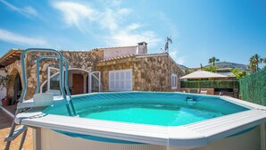 Une piscine avec un mur de pierres en arrière-plan, une échelle en métal et un ciel bleu dégagé.