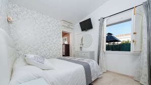 Une chambre à coucher comprenant un lit, une table de chevet, un téléviseur fixé au mur, une fenêtre avec des rideaux et une vue sur l’extérieur.