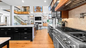A modern kitchen with a central island, black cabinetry, a stainless steel stove, and a marble backsplash. - The Grand on Greenbay-7 Bedrooms Sleeps 20 Modern new Build (Mooresville)