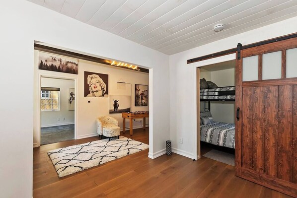 A room with a bunk bed, a desk, a chair, and artwork on the walls.