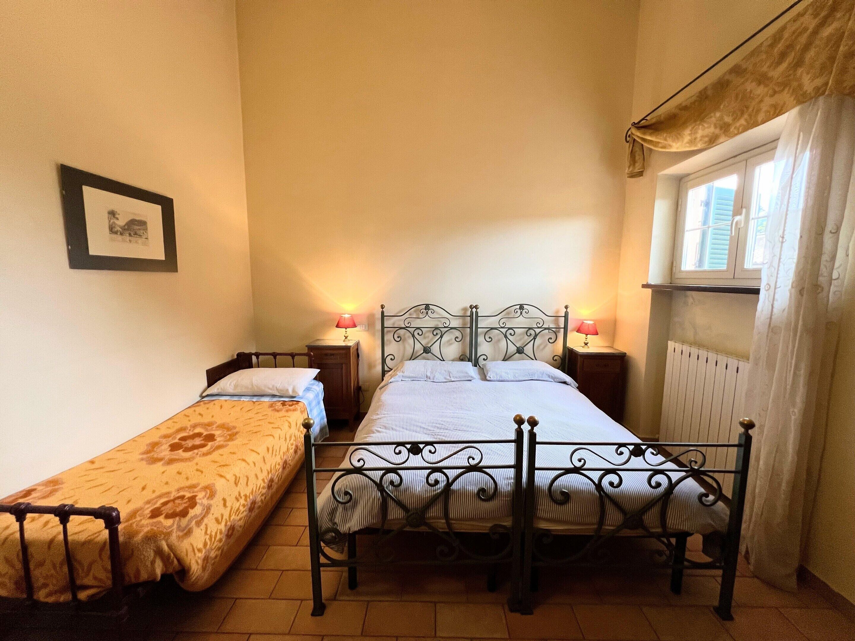 Un dormitorio con dos camas individuales, una ventana con cortinas, un radiador y un cuadro en la pared.