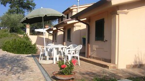 Un patio exterior con una mesa, sillas, una planta en maceta y un paraguas verde.