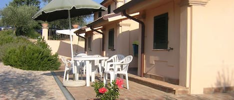 Une terrasse extérieure avec une table et des chaises, une plante en pot et un parasol vert.