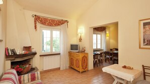 Una sala de estar acogedora con chimenea, un televisor sobre un mueble de madera, una zona de comedor con mesa y sillas, y un cuadro en la pared.