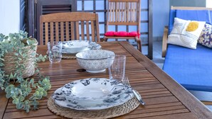 A wooden dining table set with plates, bowls, and glasses, surrounded by chairs and a blue sofa. - La Corte del Gallo by Interhome (Budoni)