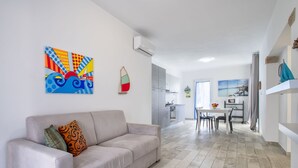 Een moderne woonkamer met een bank, een eethoek met tafel en stoelen, en een keuken op de achtergrond.