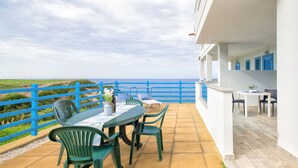 Een terras met een tafel en stoelen, uitzicht op zee, en een blauwe omheining.
