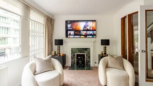 A living room with two armchairs, a fireplace, a TV mounted above it, and a door on the right. - Extravagant 6 Bedroom Mansion by Mayfair London (London)