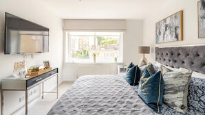 A modern bedroom with a large bed, a TV, a desk, and a window with a city view. - Extravagant 6 Bedroom Mansion by Mayfair London (London)