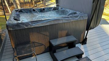 Een hottub met een houten buitenkant, een netstoel en een klein opstapkrukje op een houten terras.