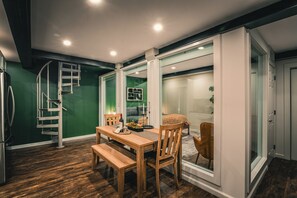 A dining area with a wooden table and chairs, a bench, a spiral staircase, and a sliding glass door leading to a bathroom.