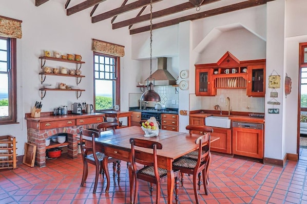 A rustic kitchen with a brick oven, wooden furniture, and a view of the outdoors.