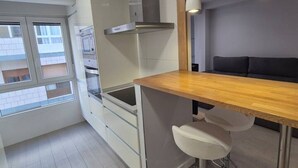 A modern kitchen with a wooden countertop, white cabinets, and a stainless steel range hood. There is a window providing a view of the outside. - 124C Apartamento moderno 2 dormitorios (Gijón)