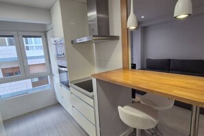 A modern kitchen with a wooden countertop, white cabinets, and a stainless steel range hood. There is a window providing a view of the outside.