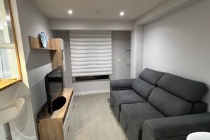 A modern living room with a grey sectional sofa, a wooden cabinet, and a window with blinds.