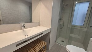 A modern bathroom with a white sink, mirror, and glass shower enclosure. - 124C Apartamento moderno 2 dormitorios (Gijón)