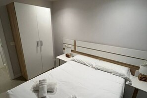 A hotel room with a bed, a nightstand, a wardrobe, and a bedside table.