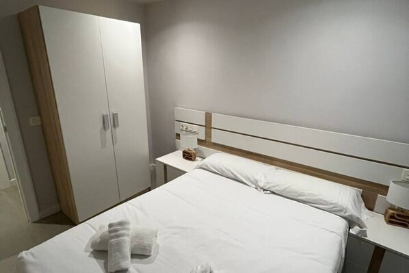 A hotel room with a bed, a nightstand, a wardrobe, and a bedside table.
