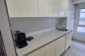 A modern kitchen with white cabinets, a stainless steel sink, and a coffee maker on the counter.